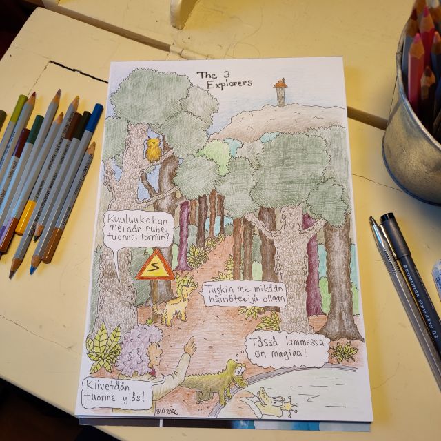 Paperille piirretty väritetty sarjakuva sivu vaaleankeltaisen klaffilipaston pöytätasolla. Arkin vieressä puuvärikyniä.